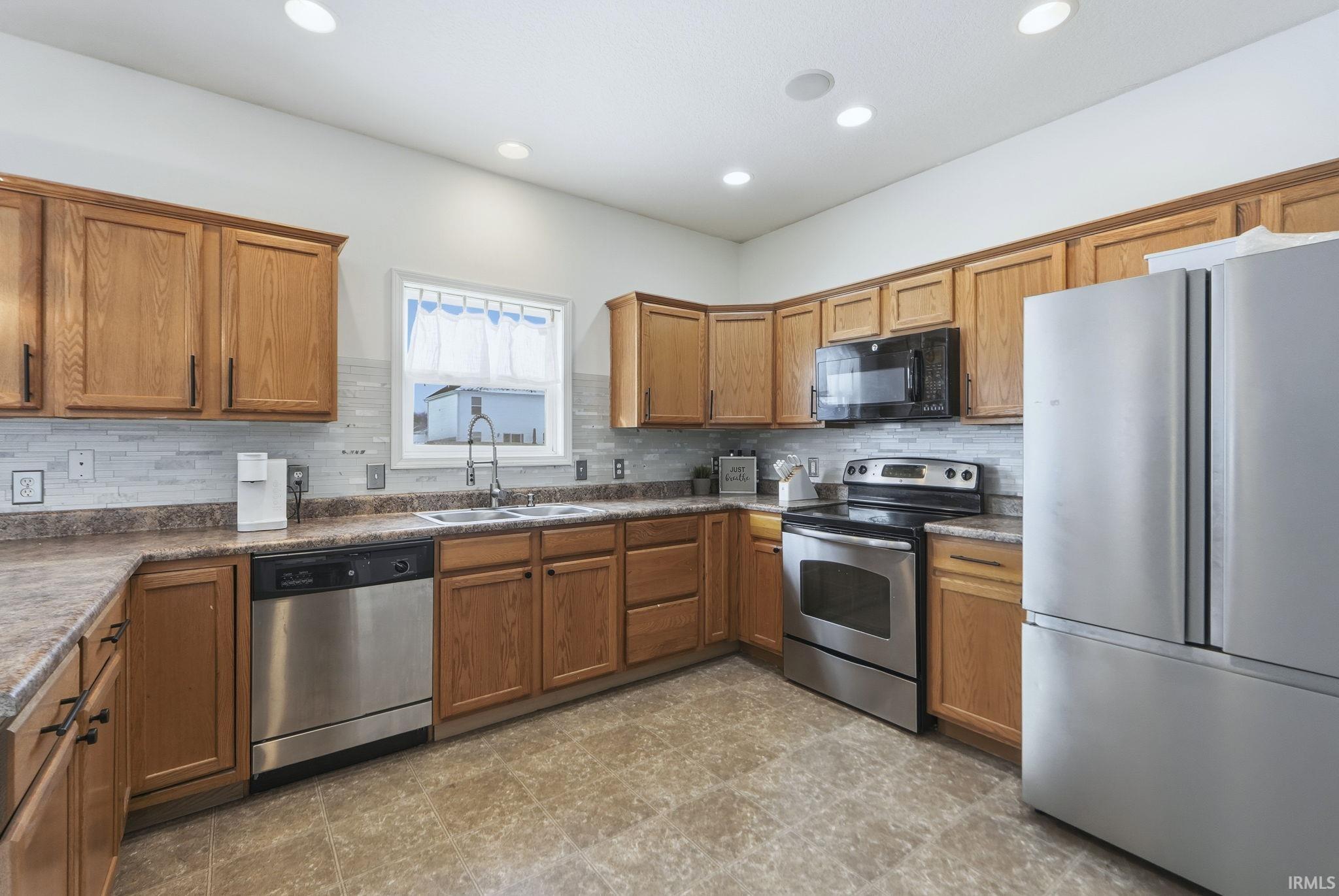 Kitchen with appliances with stainless steel finishes, brown cabinets, tasteful backsplash, dark countertops, and recessed lighting