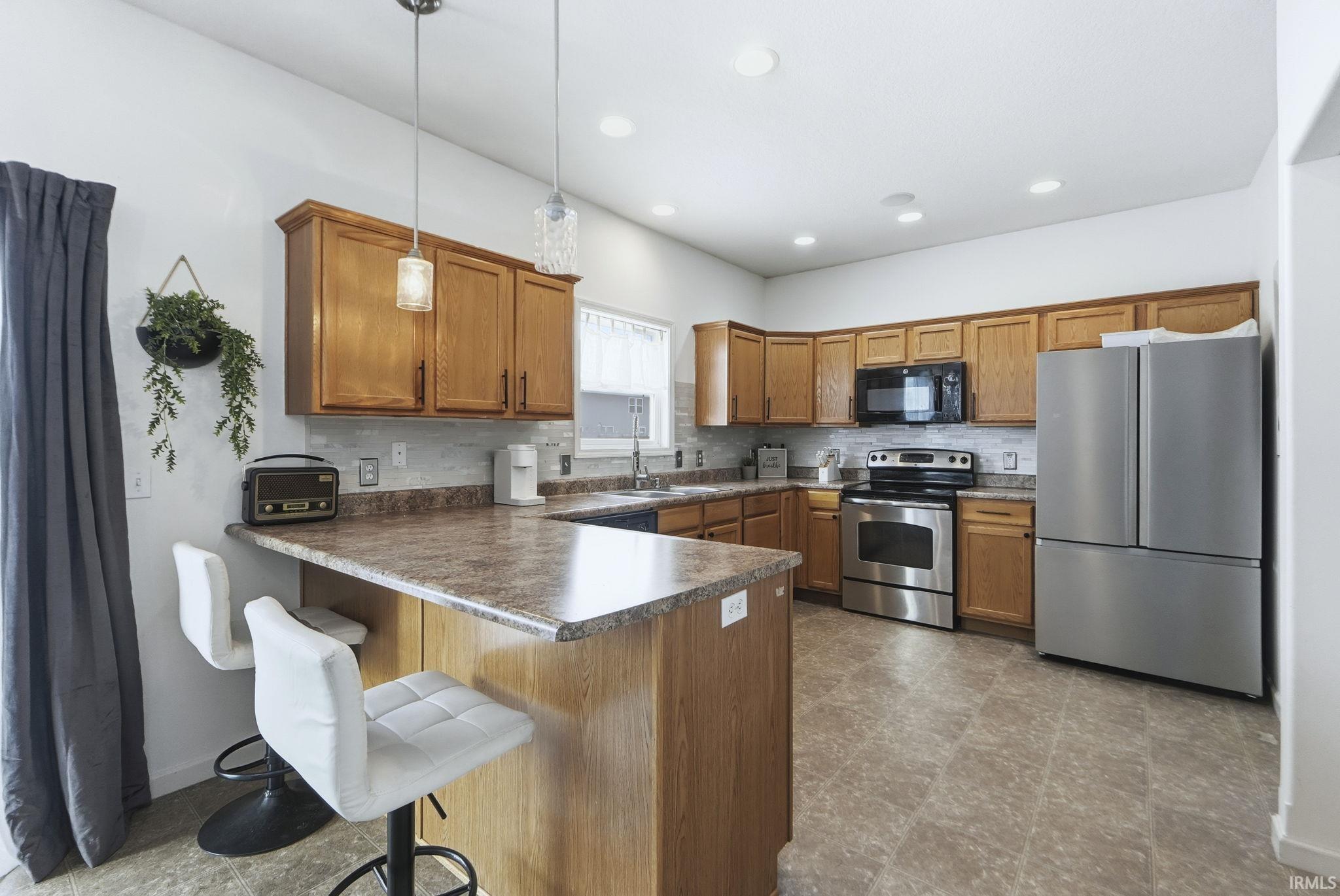 Kitchen featuring brown cabinetry, stainless steel appliances, a breakfast bar area, decorative light fixtures, and tasteful backsplash