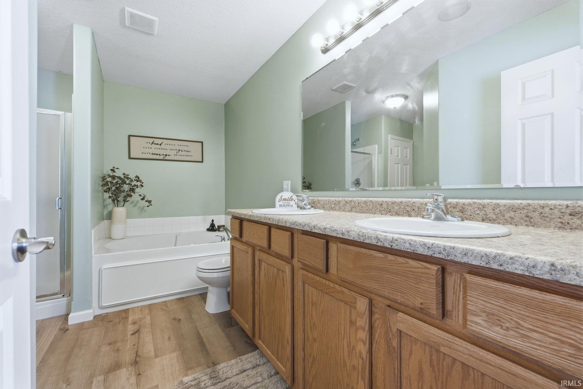 Bathroom featuring double vanity, a shower stall, a bath, light wood-style flooring, and a textured ceiling