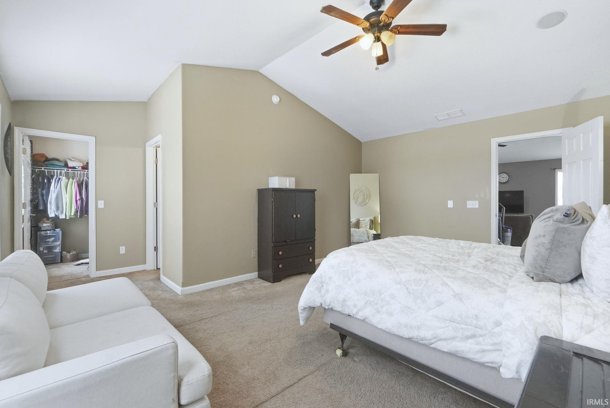 Bedroom featuring vaulted ceiling, carpet floors, a walk in closet, and a ceiling fan