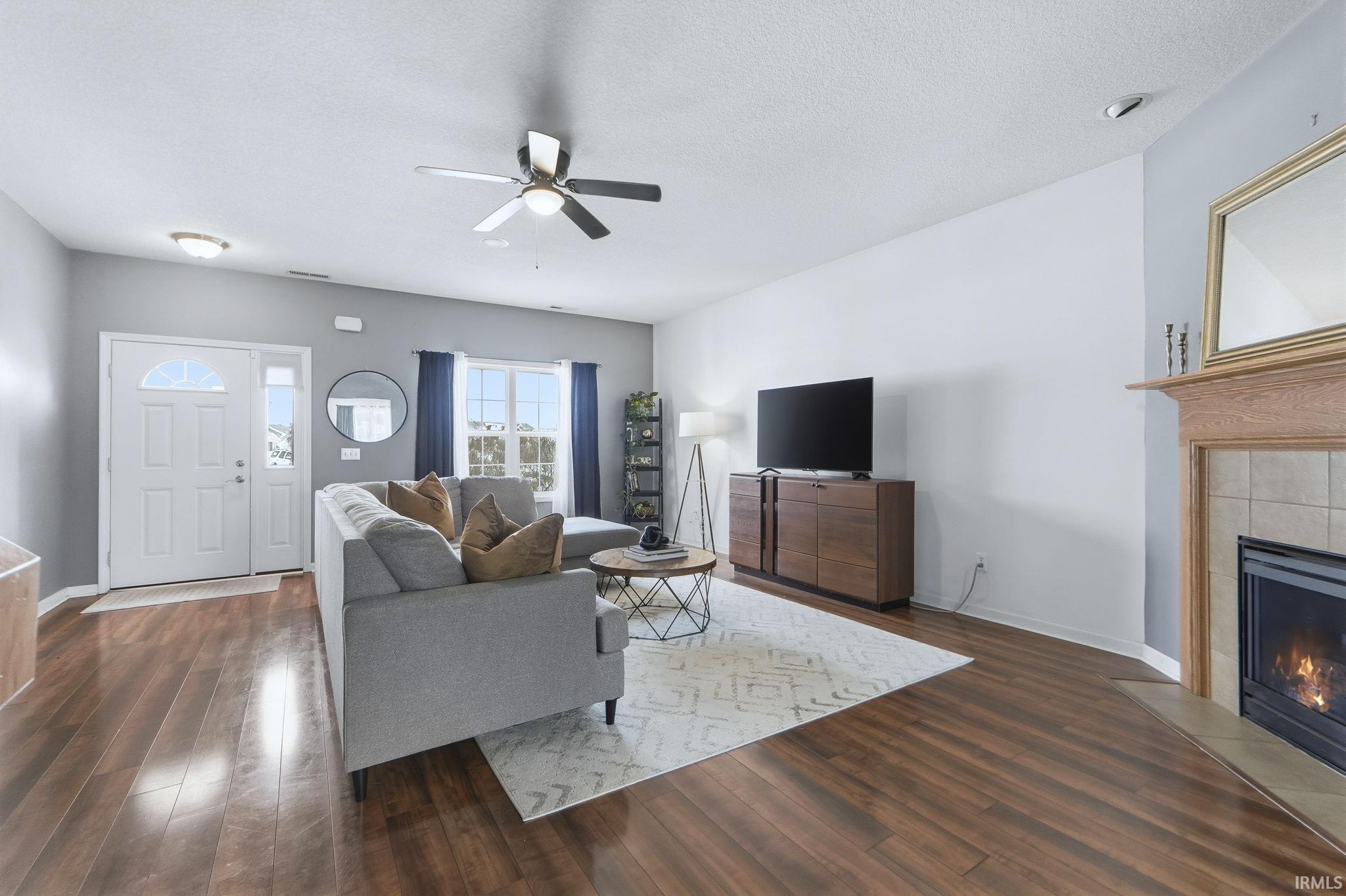 Living area featuring a tiled fireplace, ceiling fan, dark wood-type flooring, and a textured ceiling