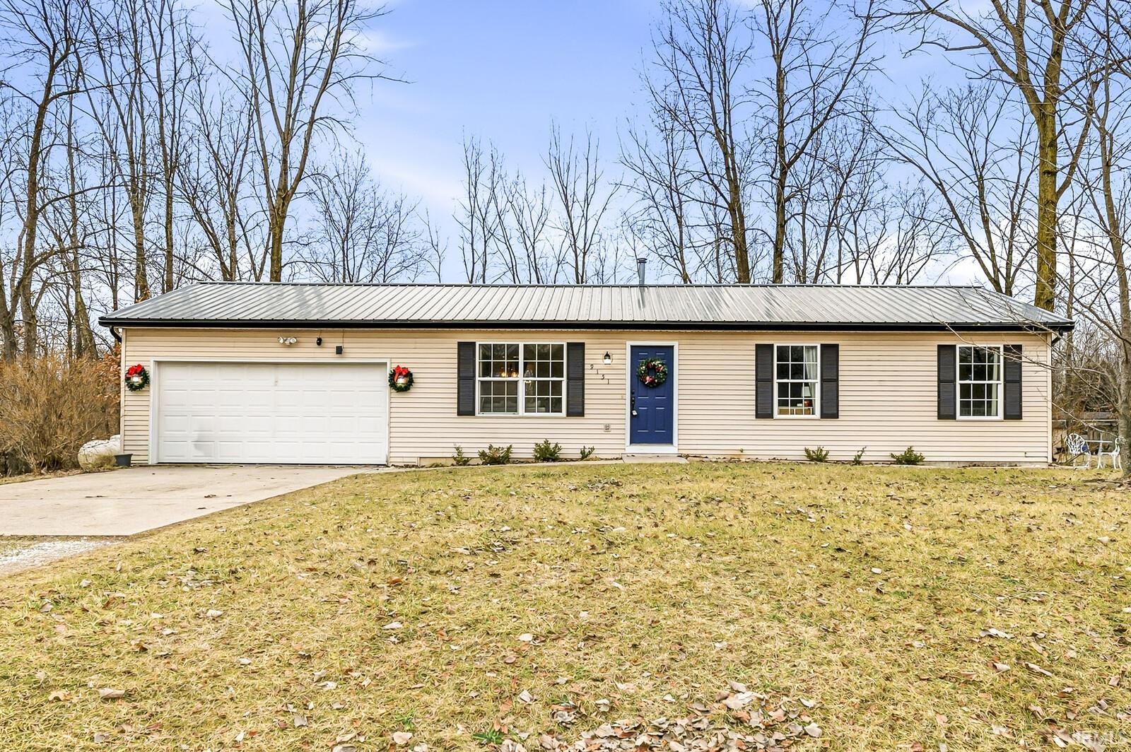 Single story home featuring concrete driveway, an attached garage, a metal roof, and a front lawn