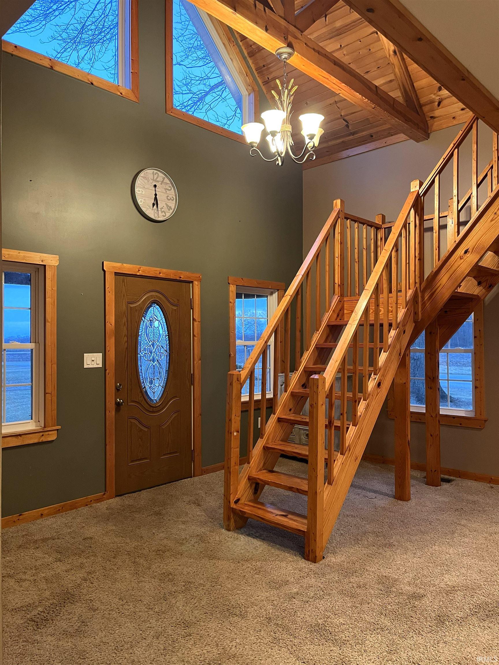 Foyer entrance with stairway, high vaulted ceiling, carpet floors, a chandelier, and a wooden ceiling with exposed beams