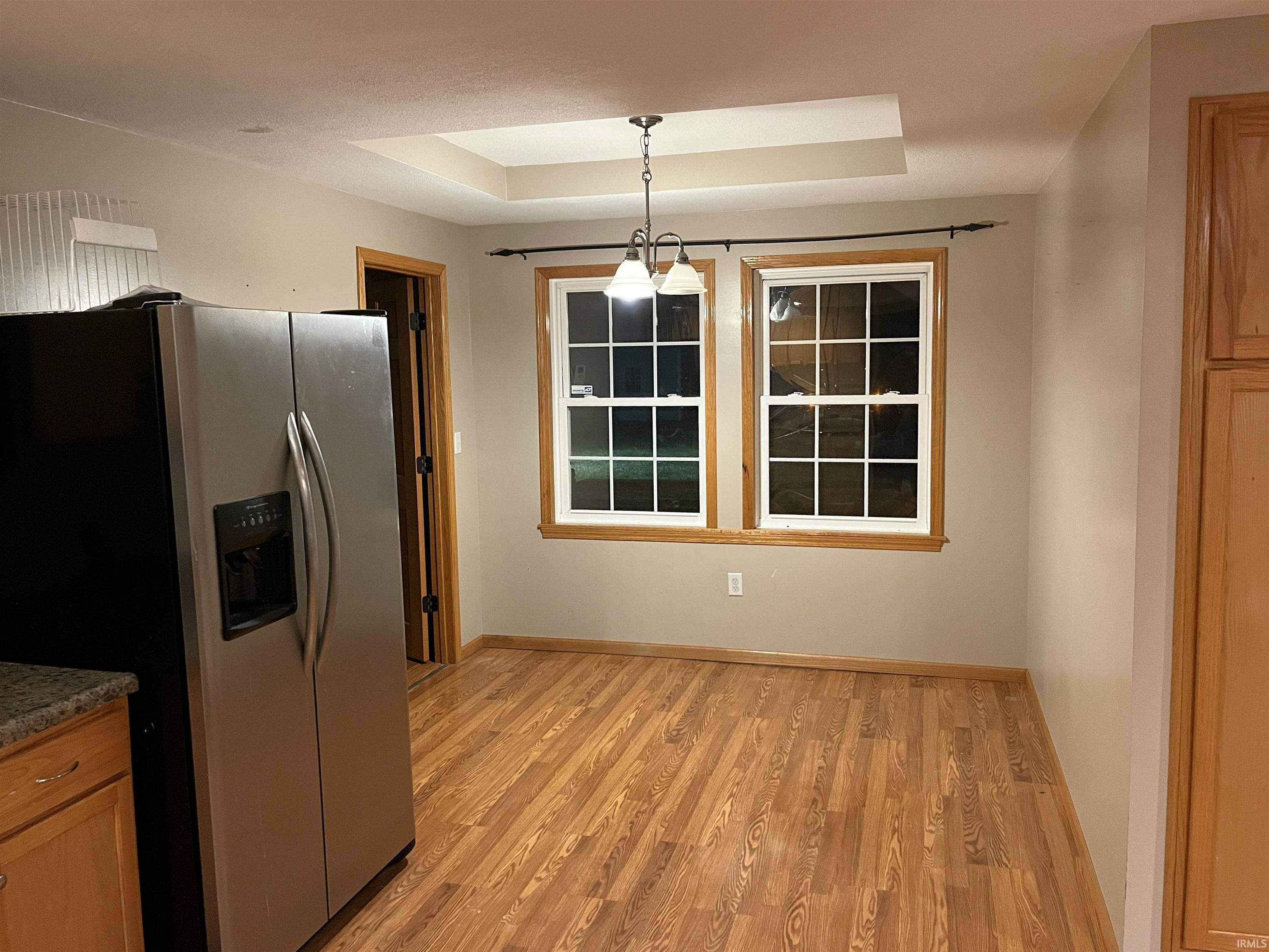Kitchen with stainless steel fridge, a raised ceiling, pendant lighting, light wood-type flooring, and brown cabinetry