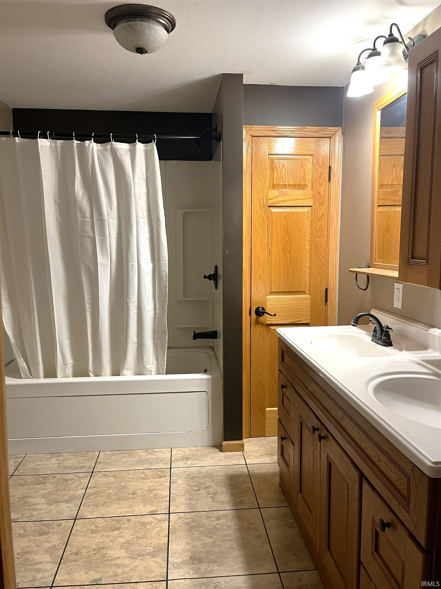 Full bathroom with shower / bathtub combination with curtain, light tile patterned flooring, double vanity, and a textured ceiling