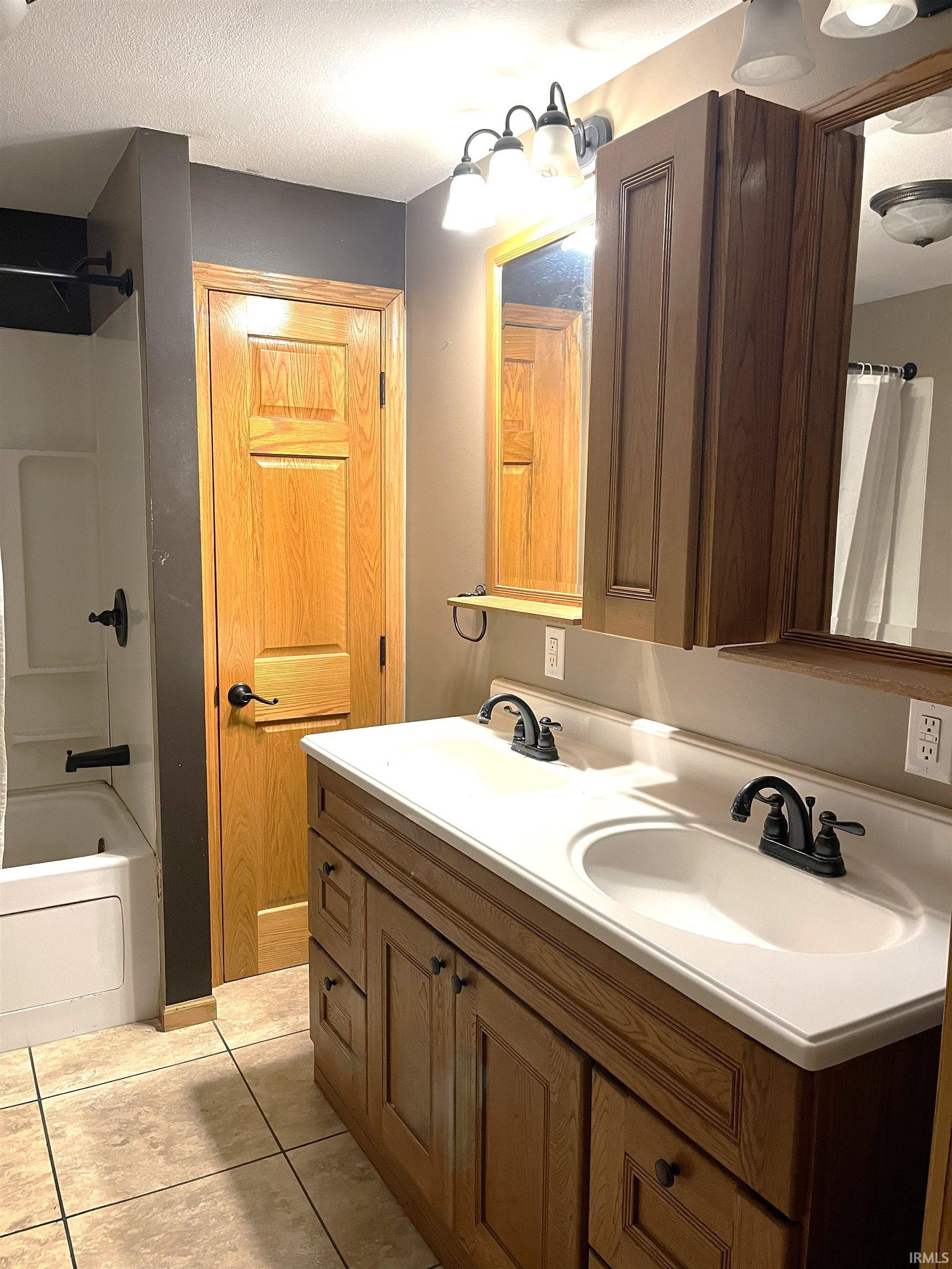 Bathroom featuring shower / tub combo with curtain, double vanity, light tile patterned flooring, and a textured ceiling