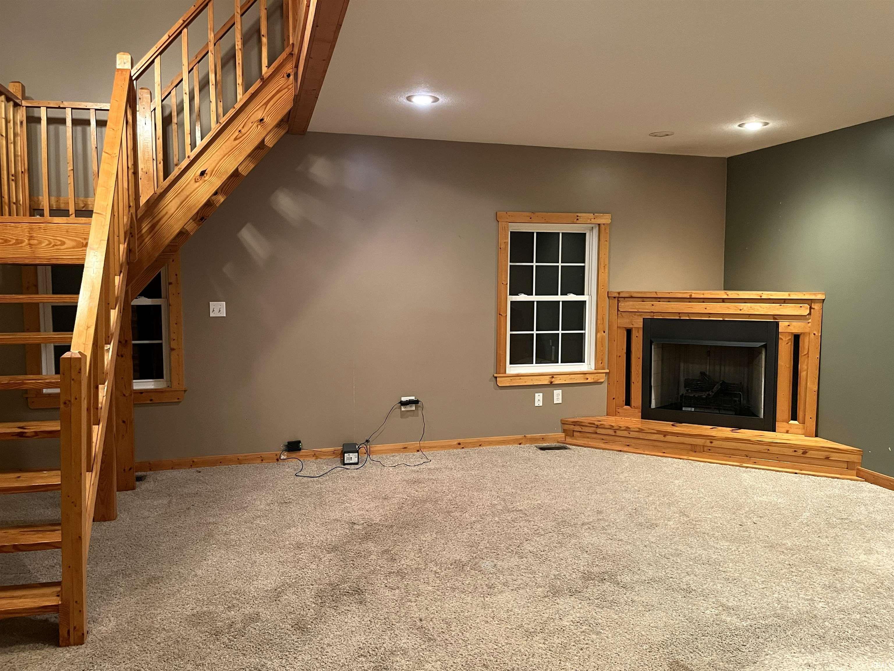 Unfurnished living room with carpet floors, stairway, a fireplace with raised hearth, and recessed lighting