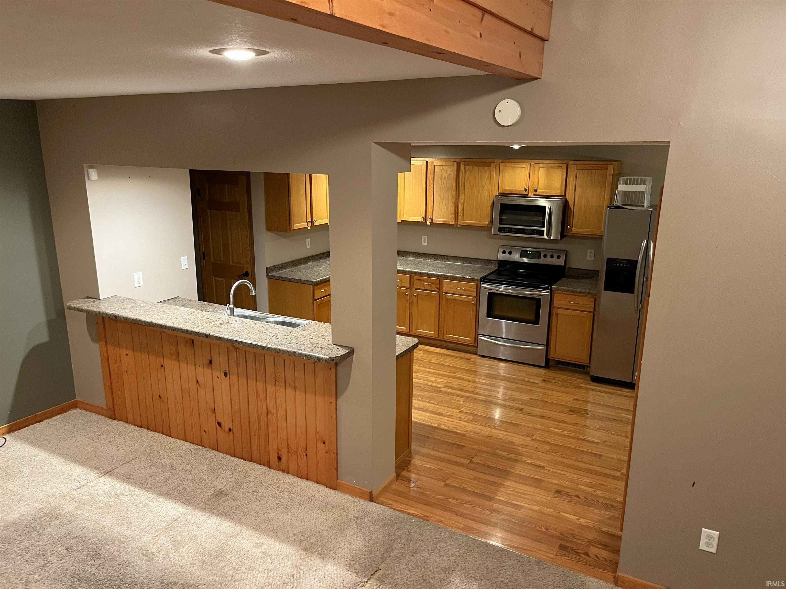 Kitchen featuring stainless steel appliances, a peninsula, light colored carpet, light stone counters, and brown cabinets