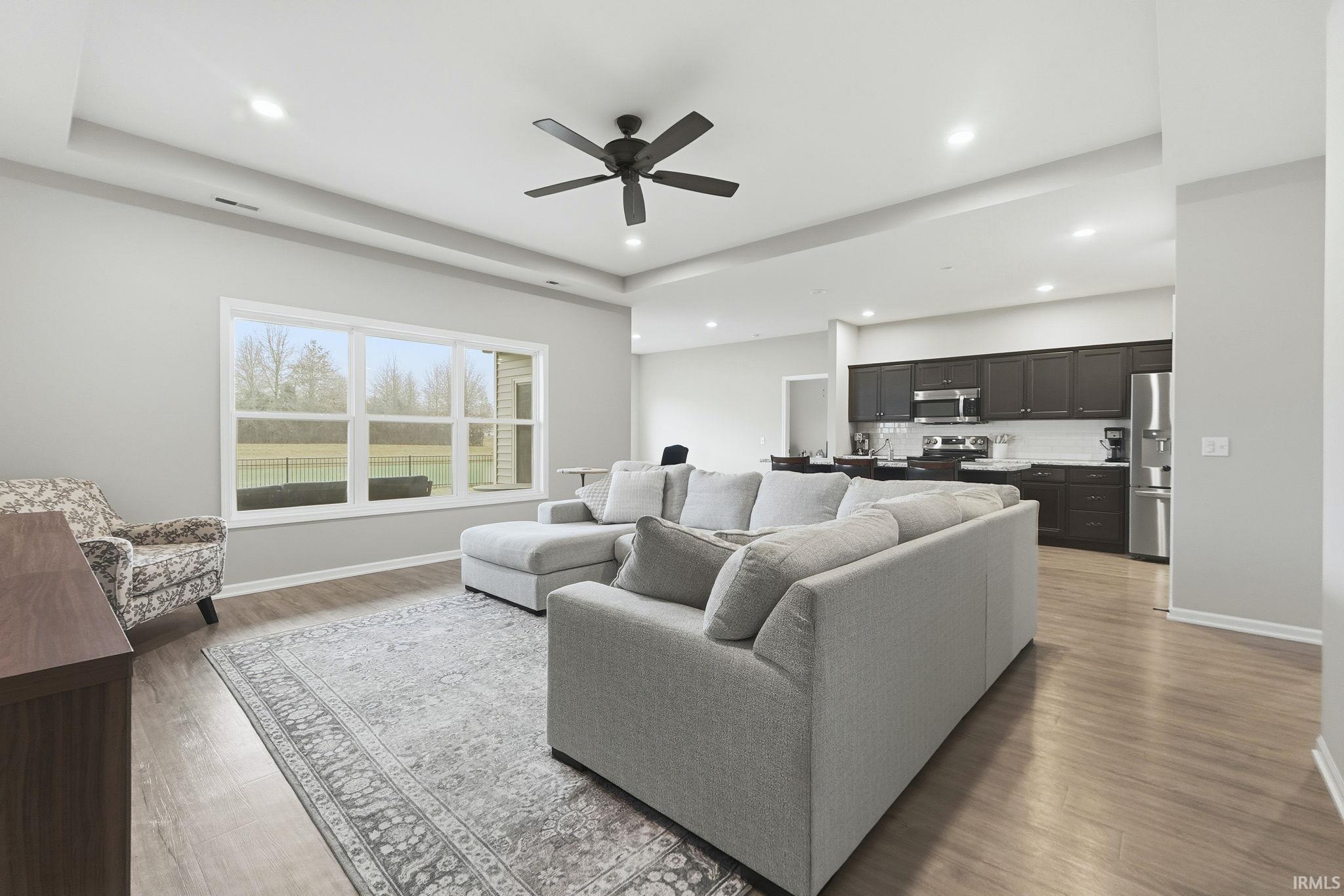 Living area with light wood-style flooring, ceiling fan, recessed lighting, and a tray ceiling
