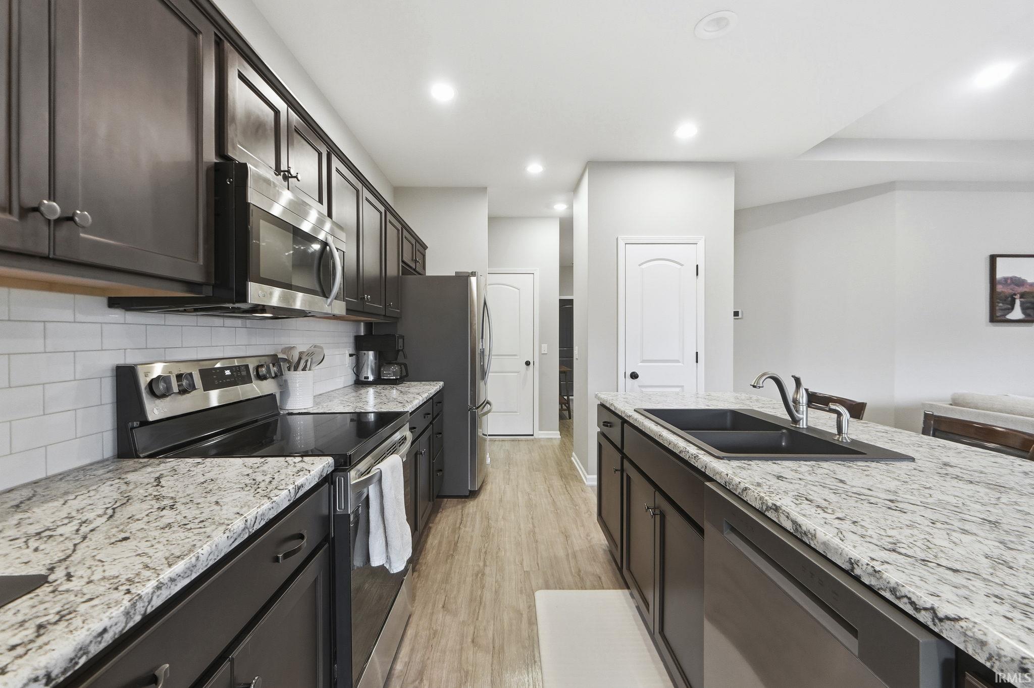 Kitchen with appliances with stainless steel finishes, light stone countertops, light wood-style flooring, recessed lighting, and tasteful backsplash