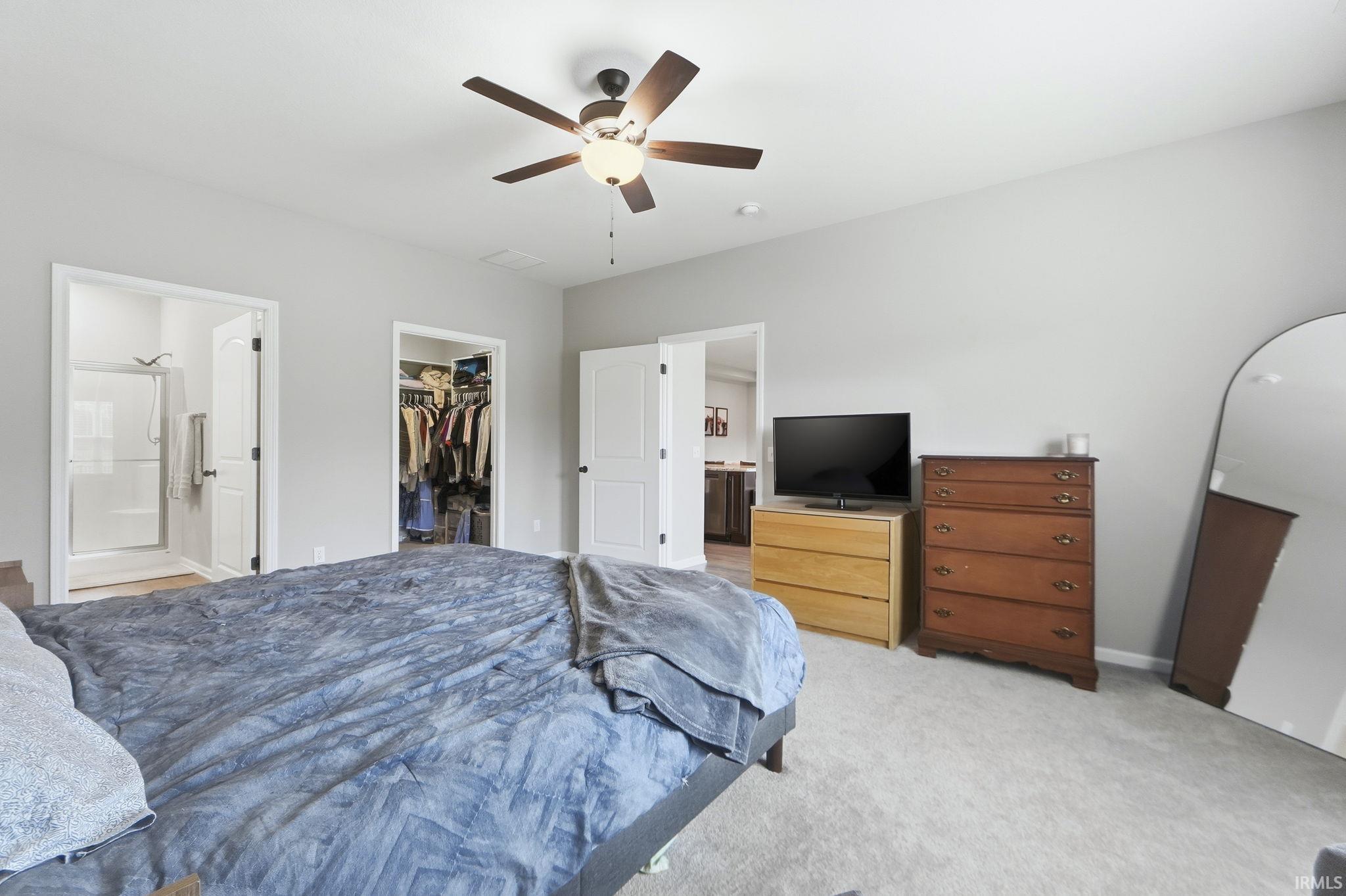 Carpeted bedroom with ensuite bath, a ceiling fan, and a walk in closet