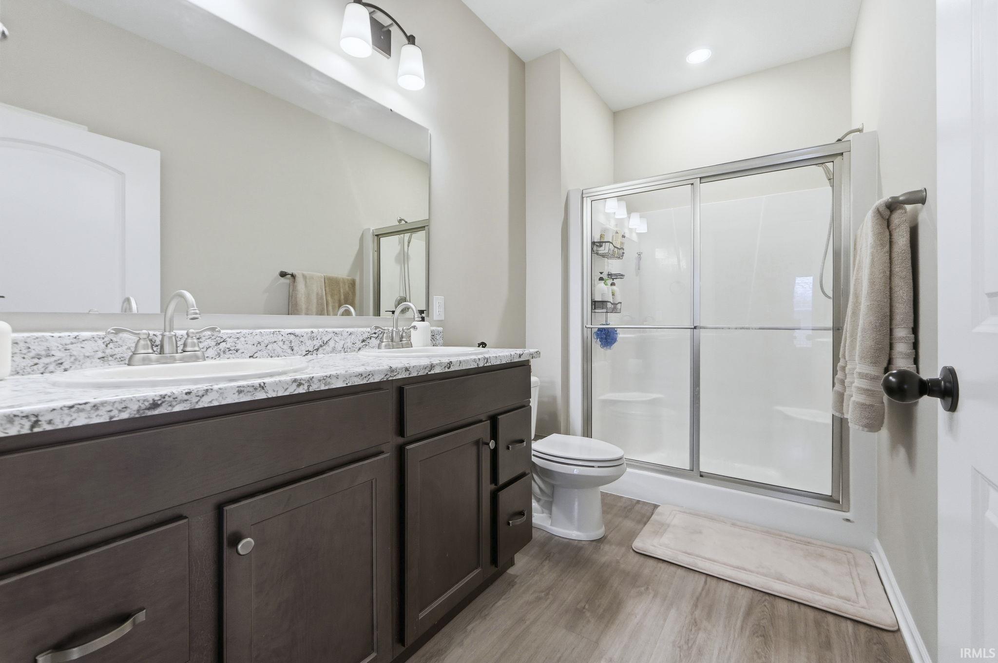 Bathroom with double vanity, a stall shower, and light wood-style flooring