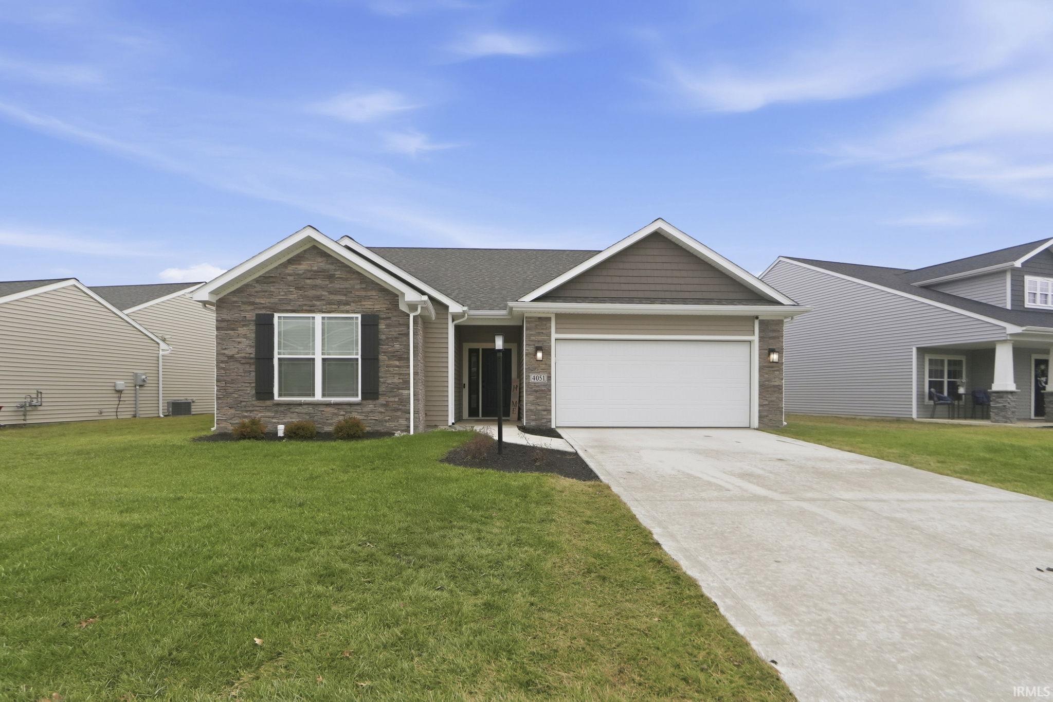 View of front facade featuring stone siding, concrete driveway, a garage, and a front lawn