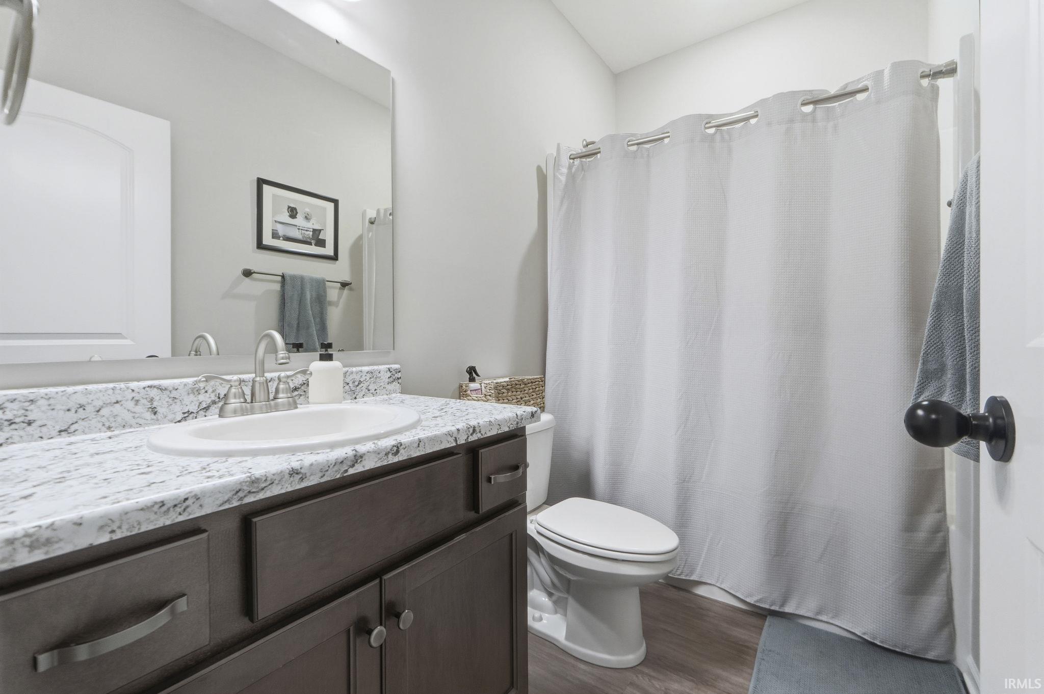 Full bath with curtained shower, vanity, and dark wood-style floors