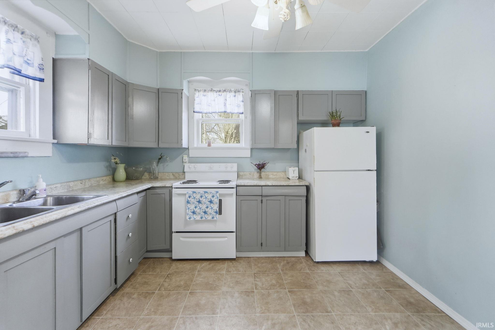 Kitchen with gray cabinetry, white appliances, light countertops, and a ceiling fan