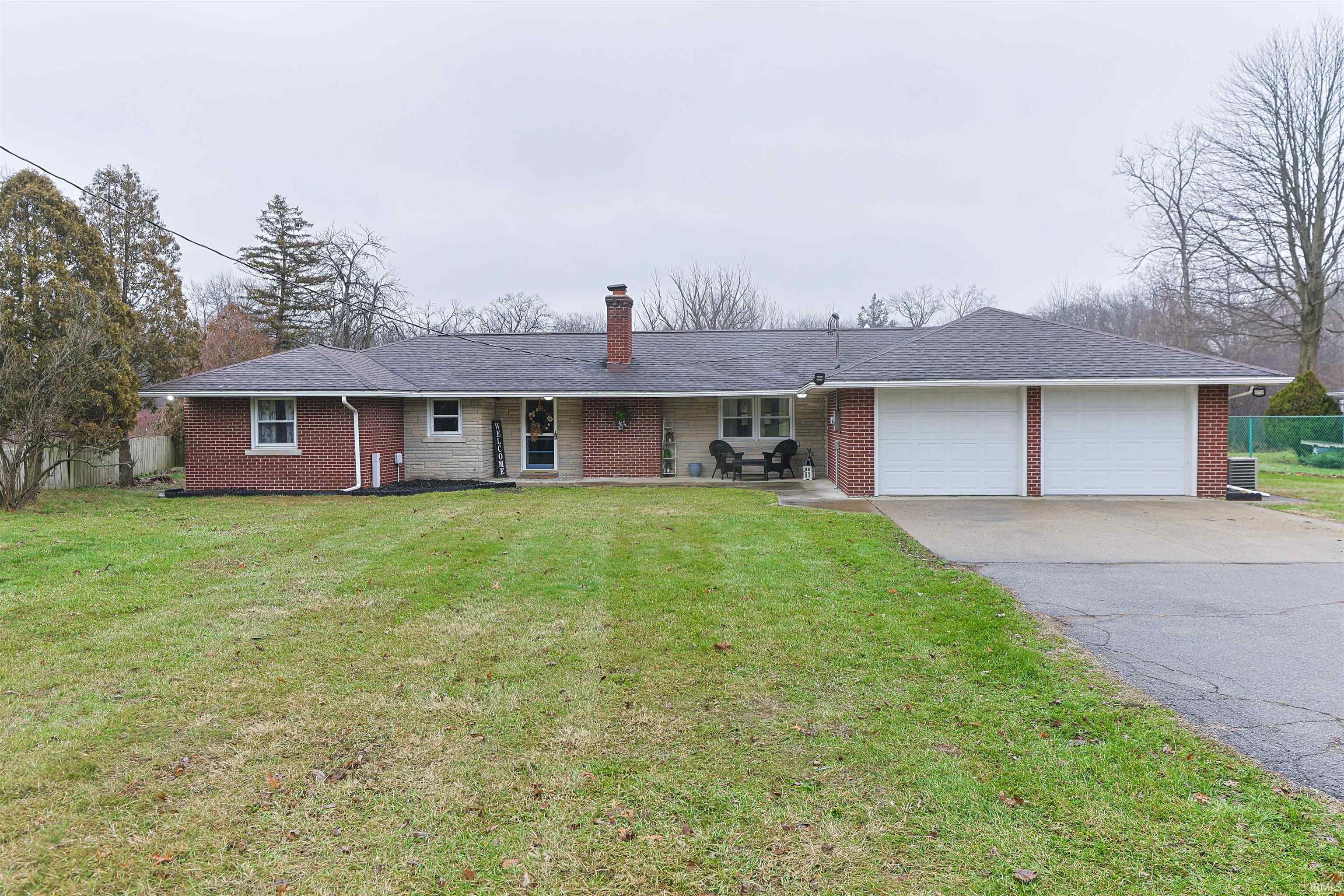 Ranch-style home featuring a chimney, a garage, asphalt driveway, brick siding, and roof with shingles