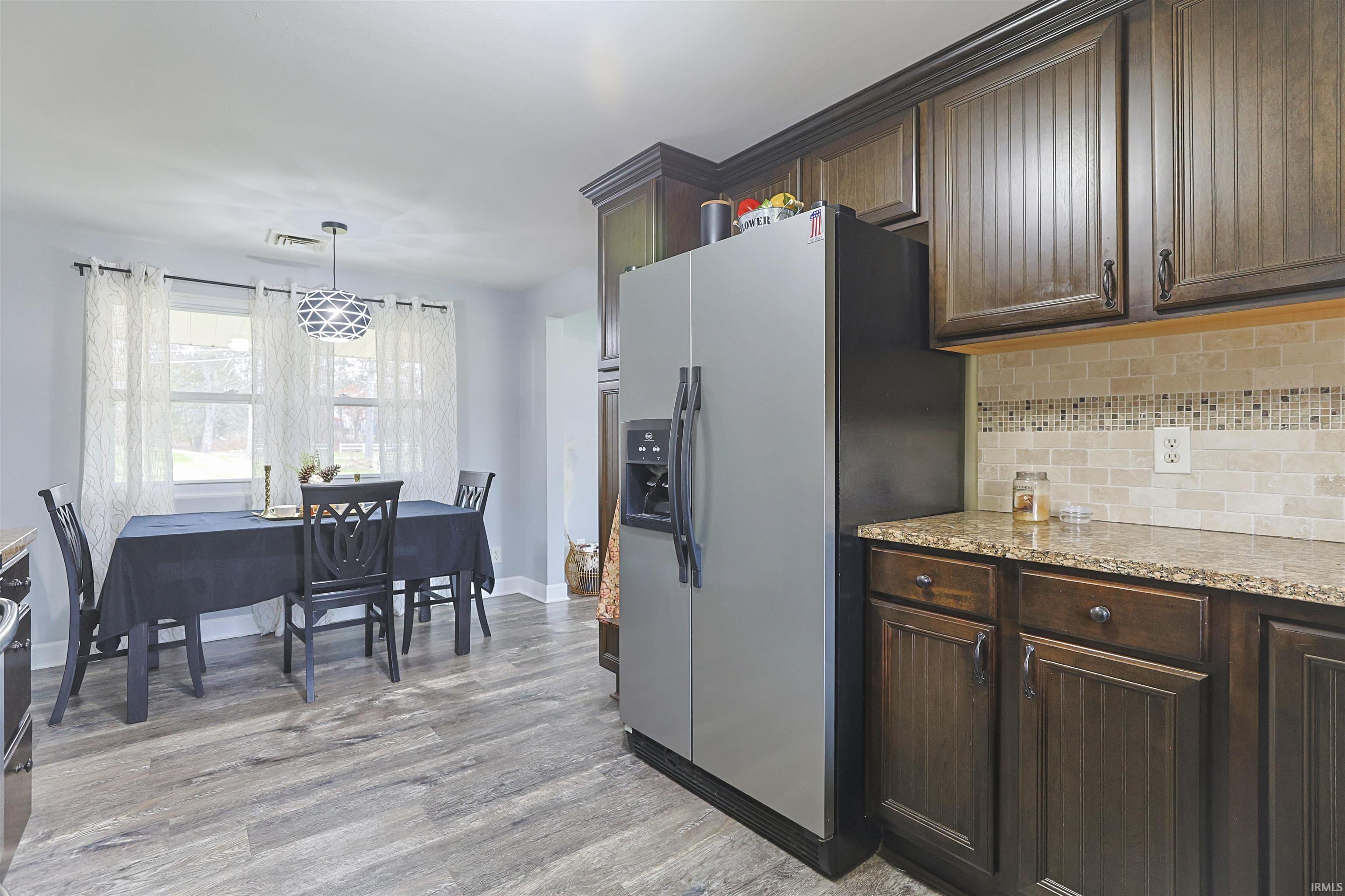 Kitchen with dark brown cabinetry, stainless steel fridge, light stone counters, and backsplash