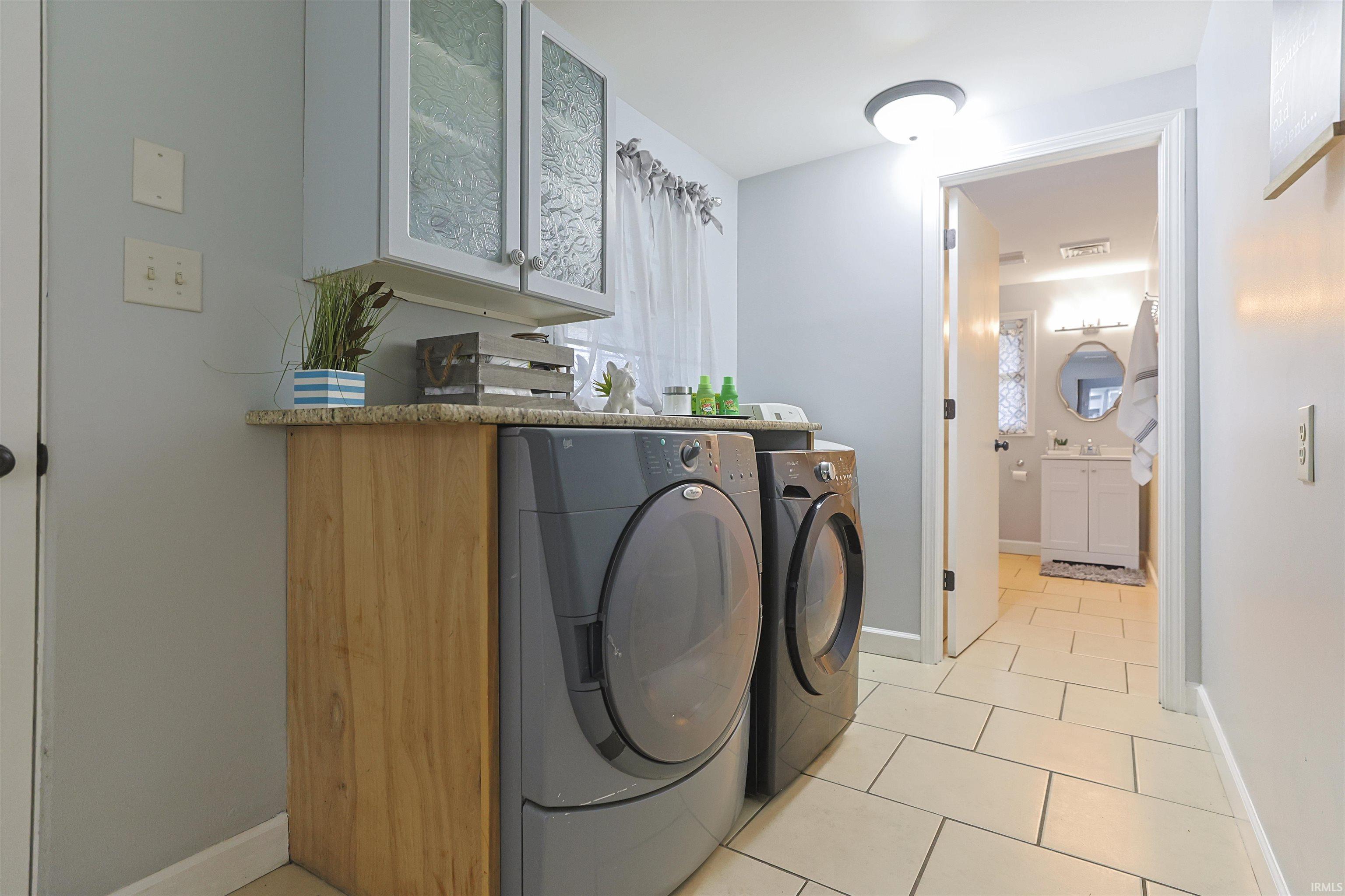 Washroom featuring light tile patterned floors, washing machine and clothes dryer, and cabinet space