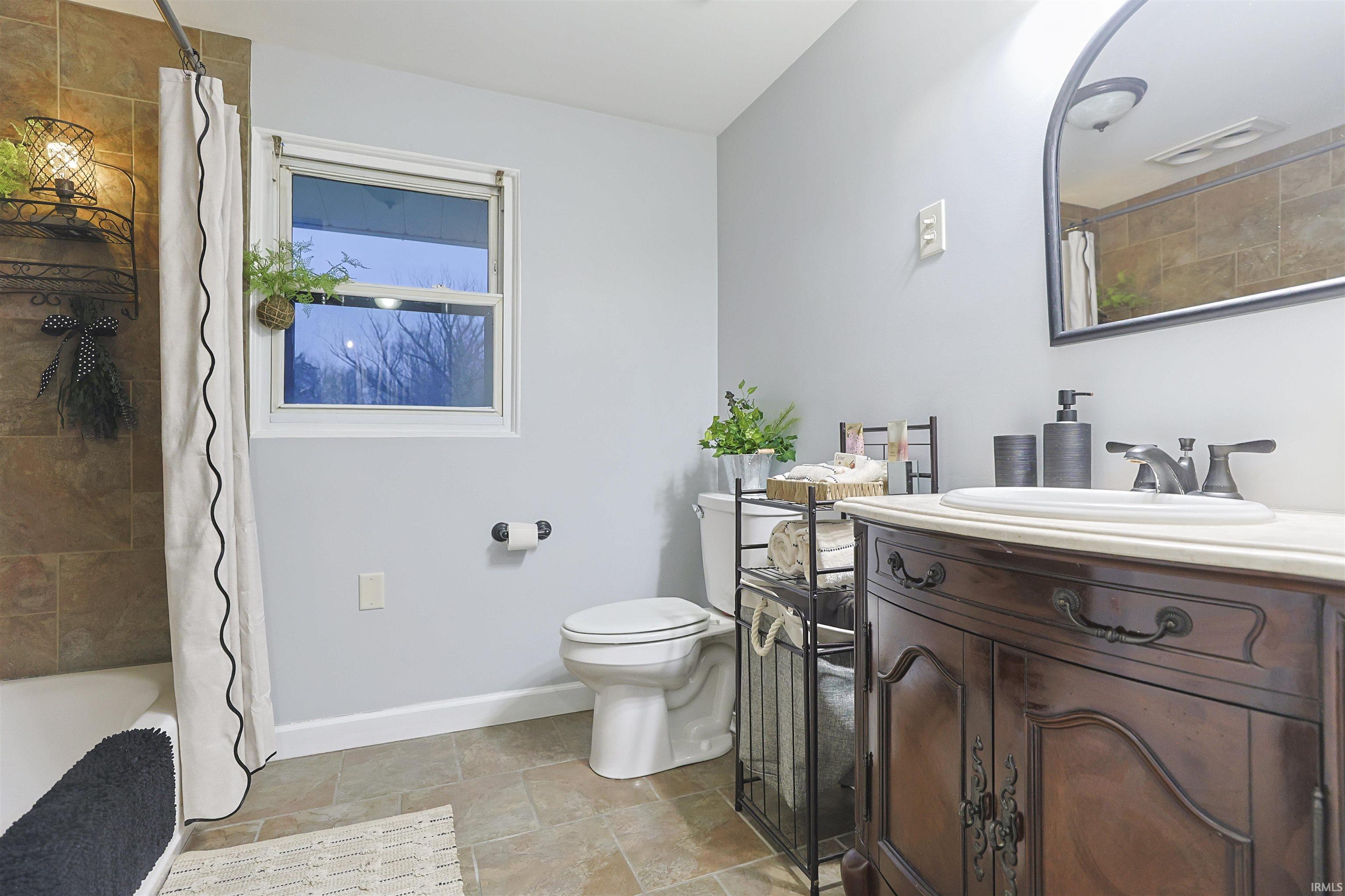 Full bathroom with vanity, shower / bath combo with shower curtain, and stone tile floors