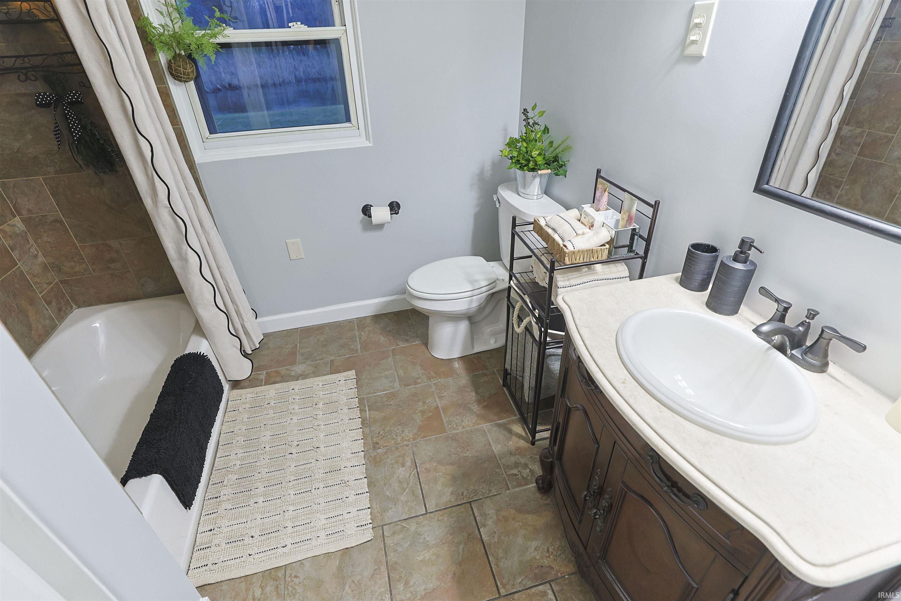 Bathroom with vanity, shower / tub combo, and stone tile flooring