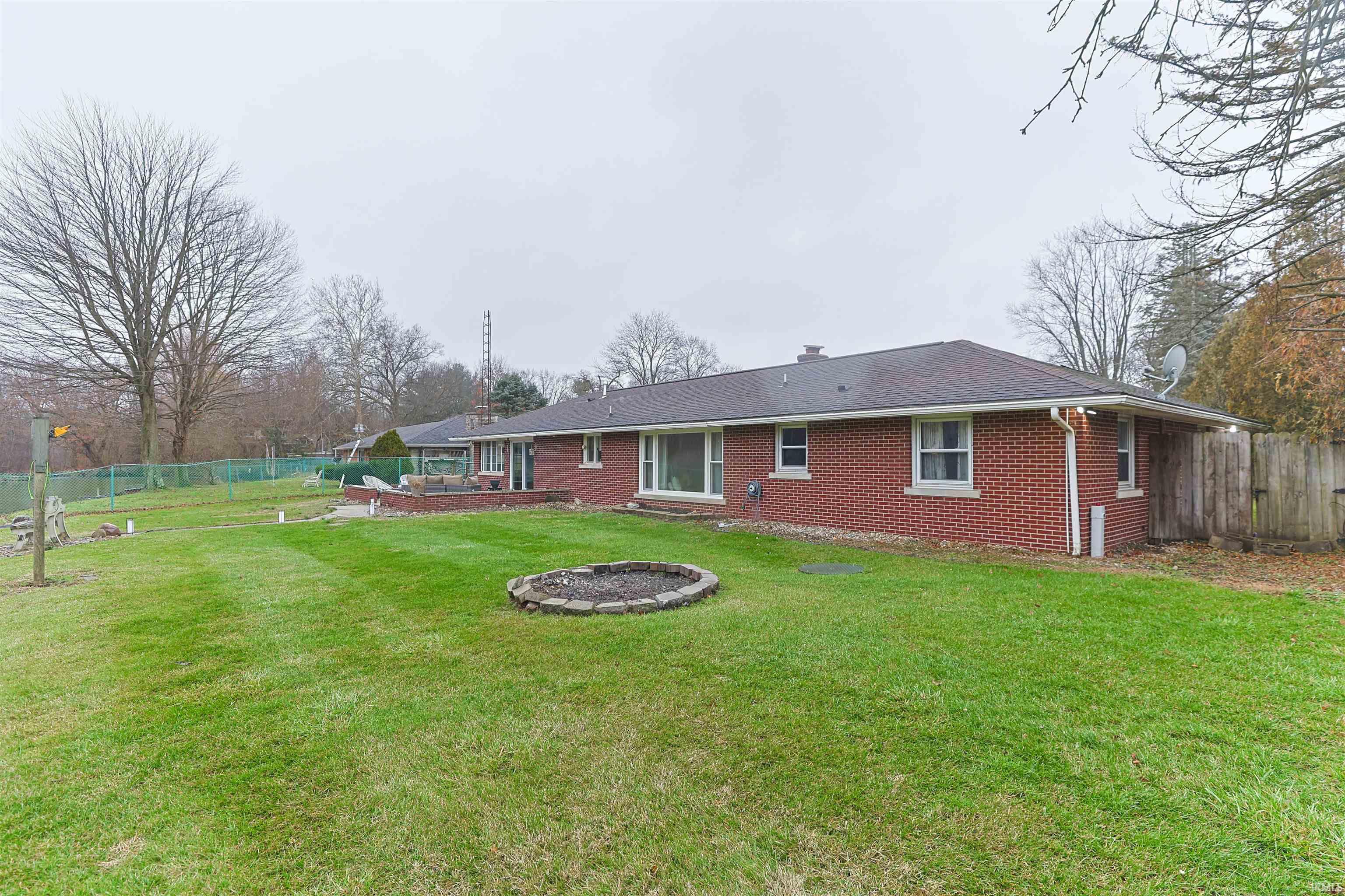 Back of house with a wooden deck, brick siding, a chimney, an outdoor living space with a fire pit, and roof with shingles
