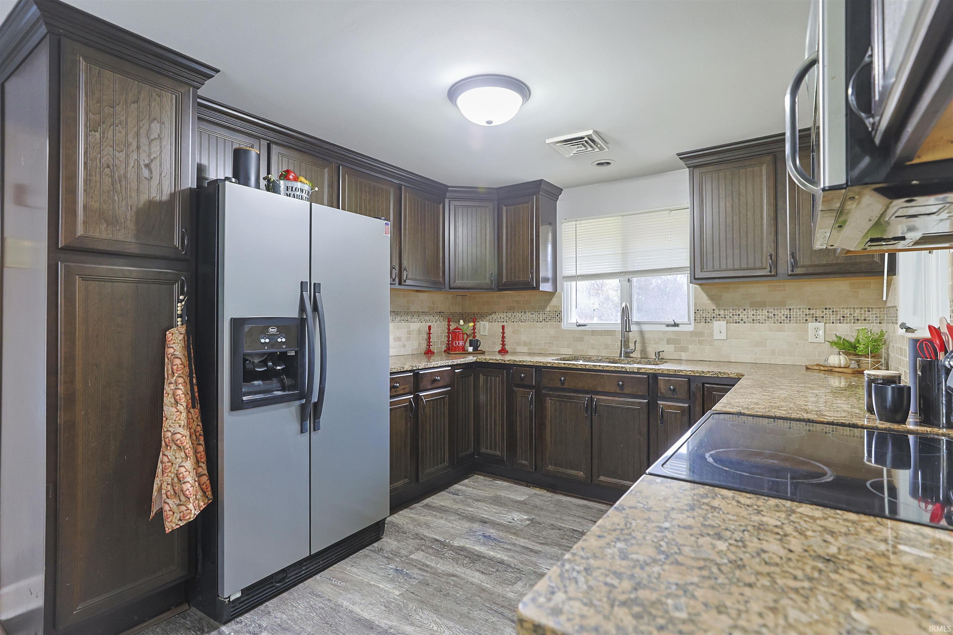 Kitchen featuring stainless steel appliances, dark brown cabinetry, light stone counters, and light wood finished floors
