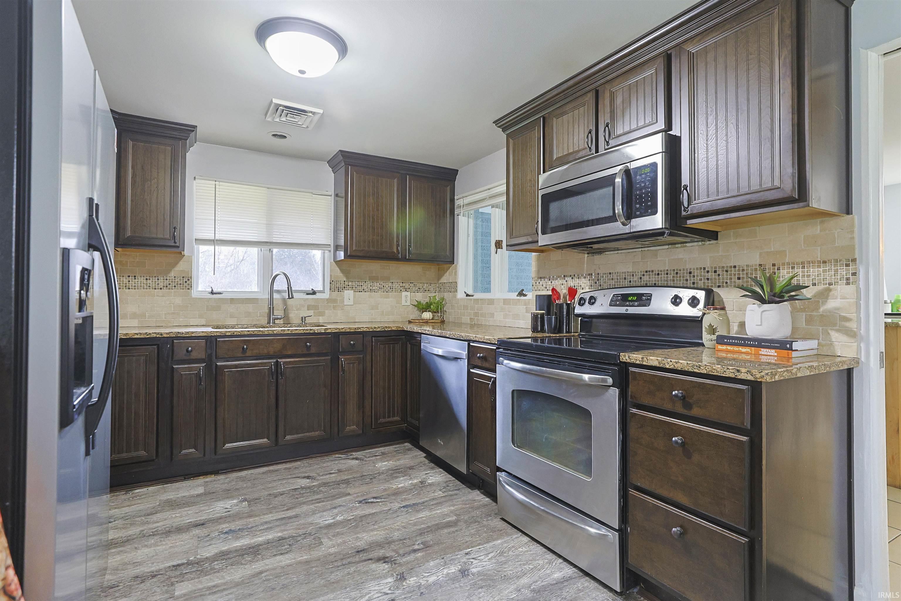 Kitchen featuring stainless steel appliances, dark brown cabinetry, light stone countertops, and decorative backsplash