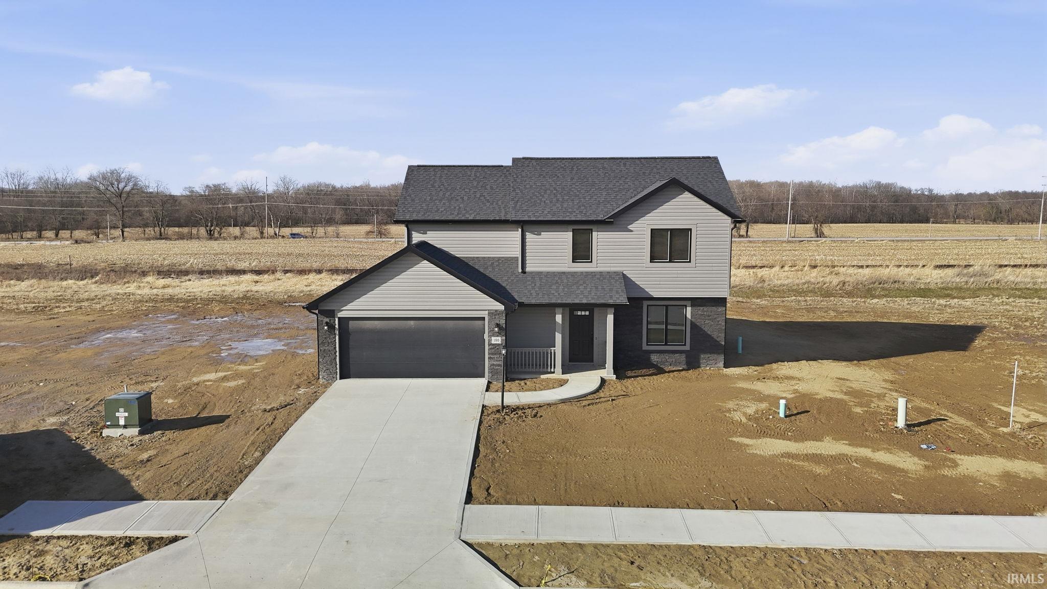 View of front of home with driveway, roof with shingles, a rural view, a porch, and a garage