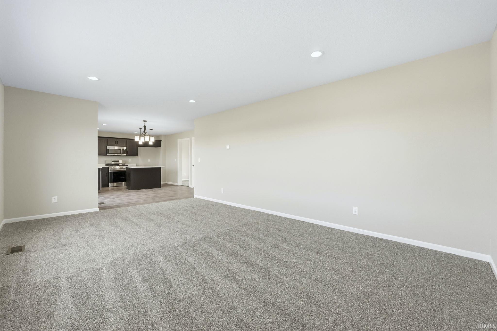 Unfurnished living room featuring light colored carpet, recessed lighting, and a chandelier