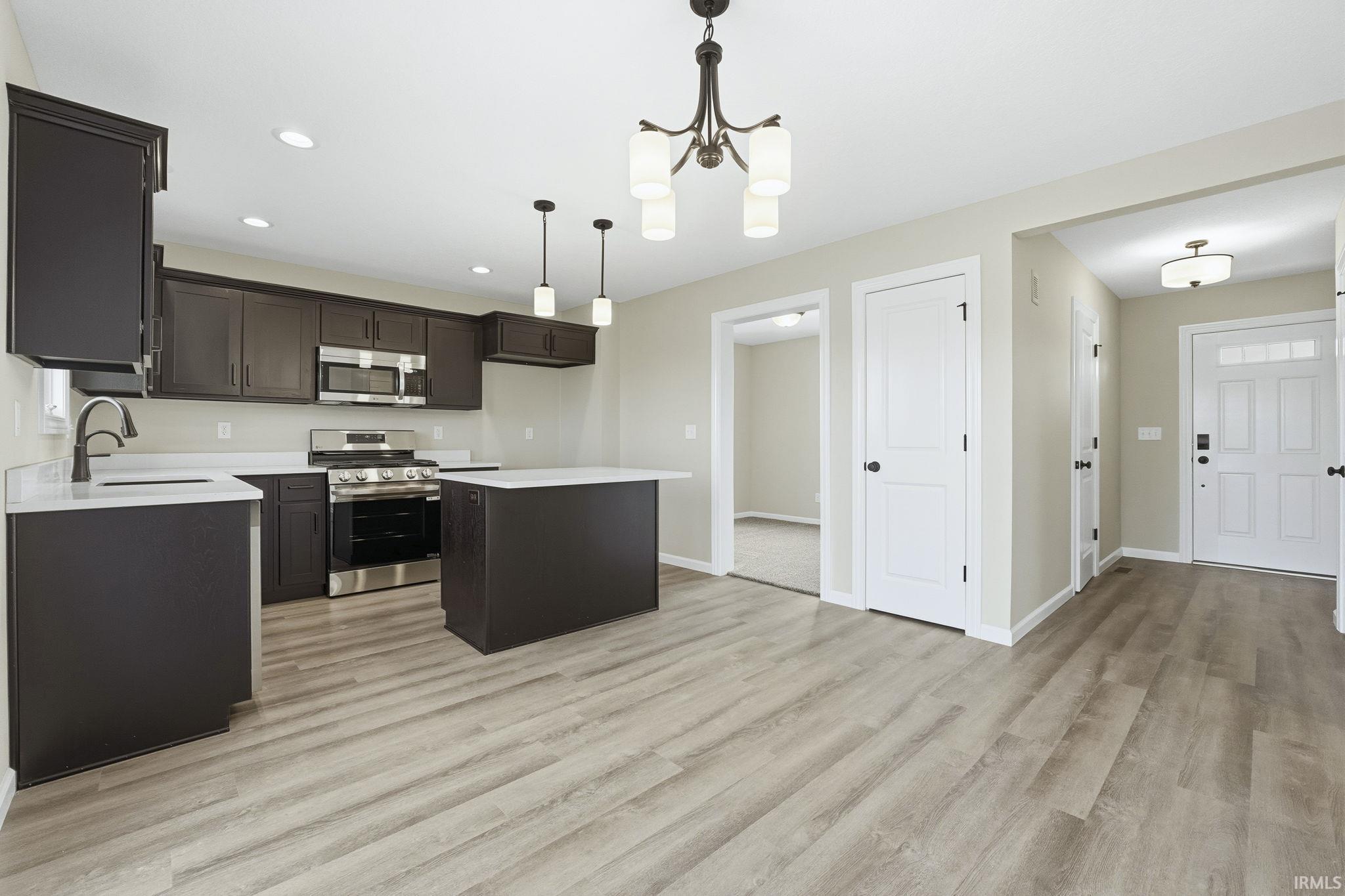 Kitchen featuring appliances with stainless steel finishes, pendant lighting, a kitchen island, a chandelier, and light wood-style flooring