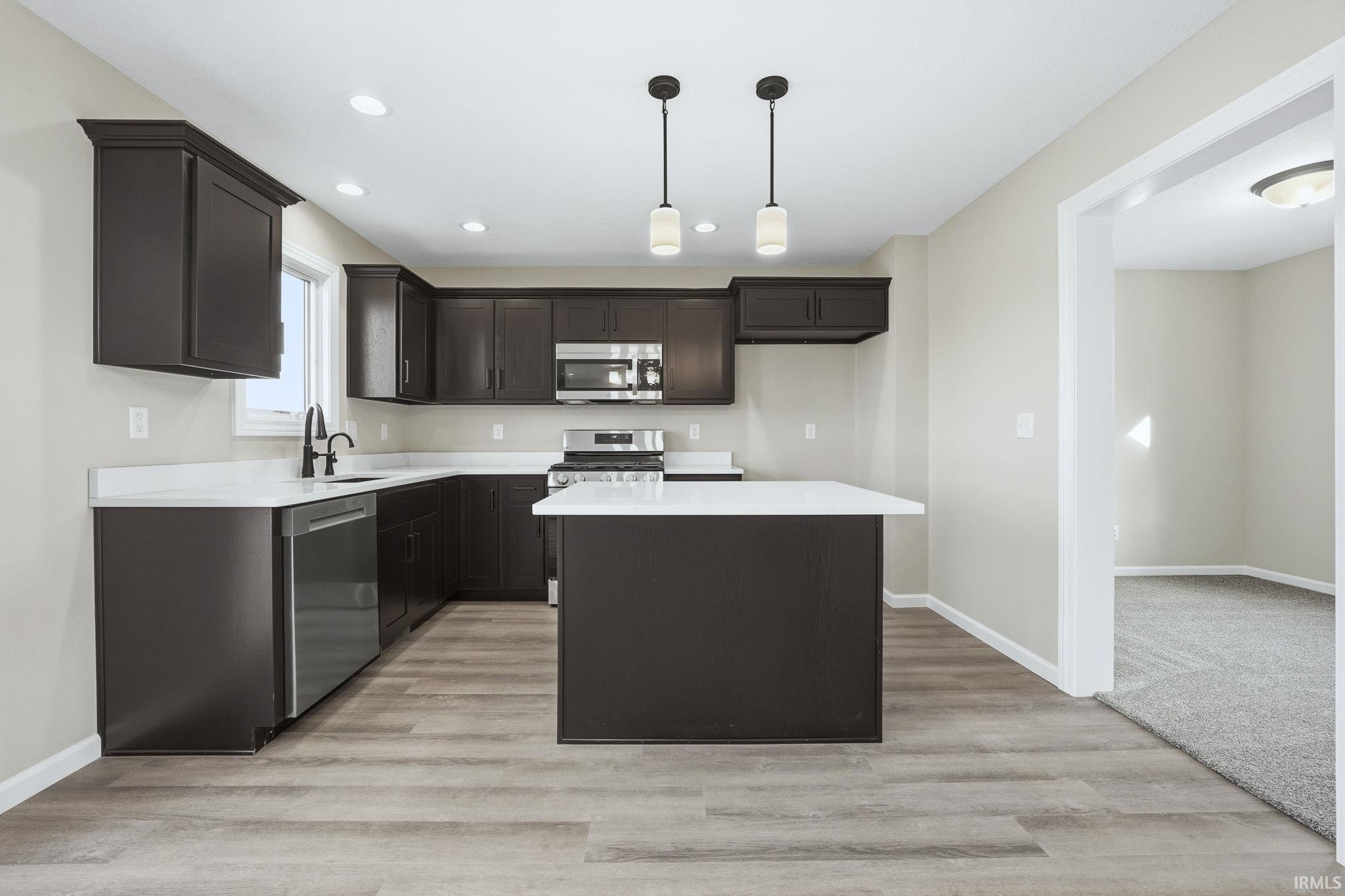 Kitchen with a center island, dark brown cabinetry, appliances with stainless steel finishes, pendant lighting, and recessed lighting