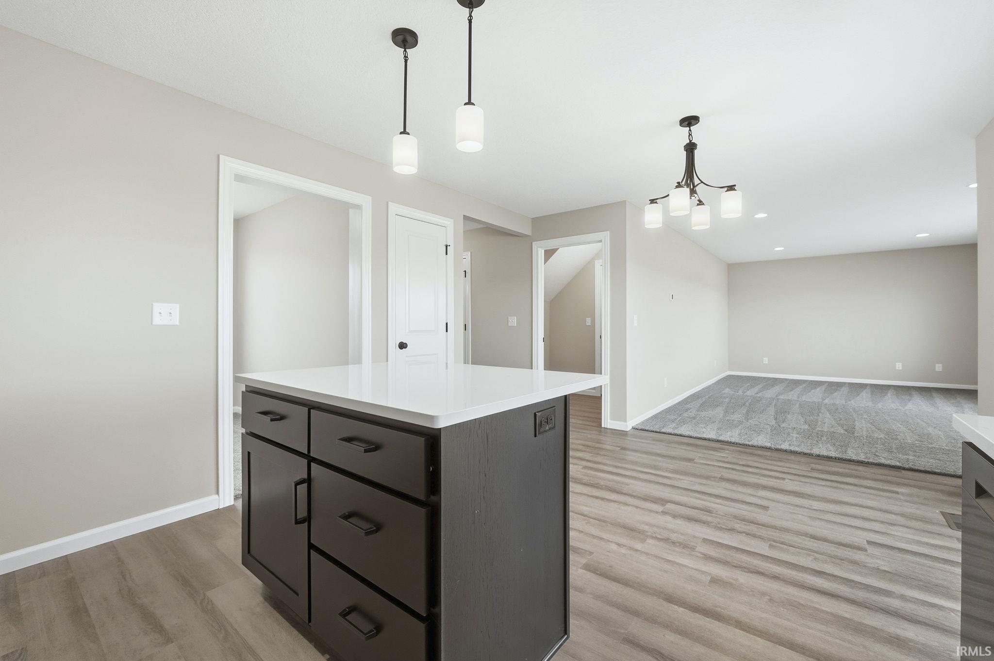Kitchen featuring hanging light fixtures, light wood-type flooring, a center island, open floor plan, and dark cabinetry